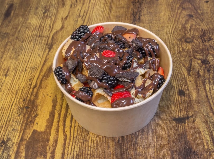 Dessert bowl filled with mini waffles, berries, crushed cookies, and chocolate drizzle.