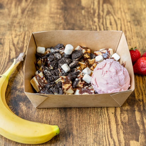 Waffle bites with chocolate sauce, cookie crumbles, marshmallows, strawberry ice cream, banana, and strawberries.