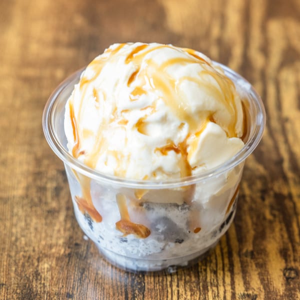 Vanilla ice cream with caramel drizzle in a clear plastic cup on a wooden table.