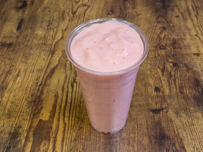 Pink smoothie in a clear plastic cup on a rustic wooden table.
