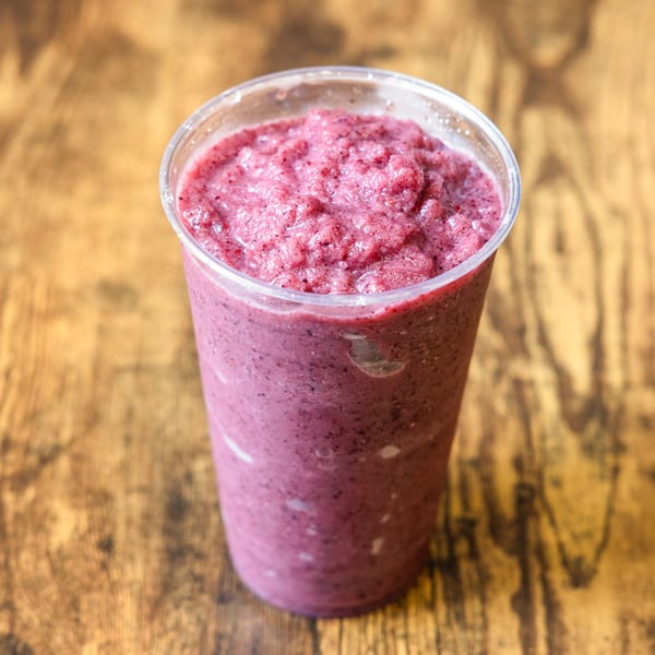 A vibrant berry smoothie in a clear plastic cup sits on a rustic wooden table.