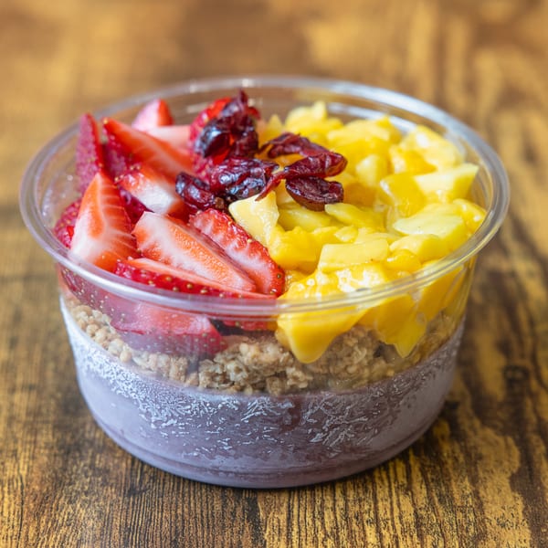 A vibrant acai bowl with strawberries, mango, and dried cranberries, on a rustic wooden table.