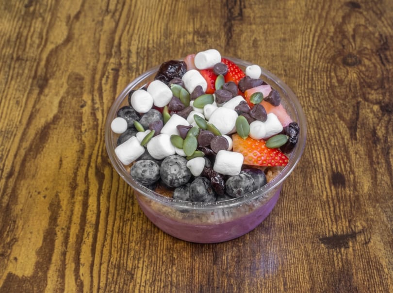 Smoothie bowl with blueberries, strawberries, marshmallows, chocolate chips, and pumpkin seeds in a clear cup.
