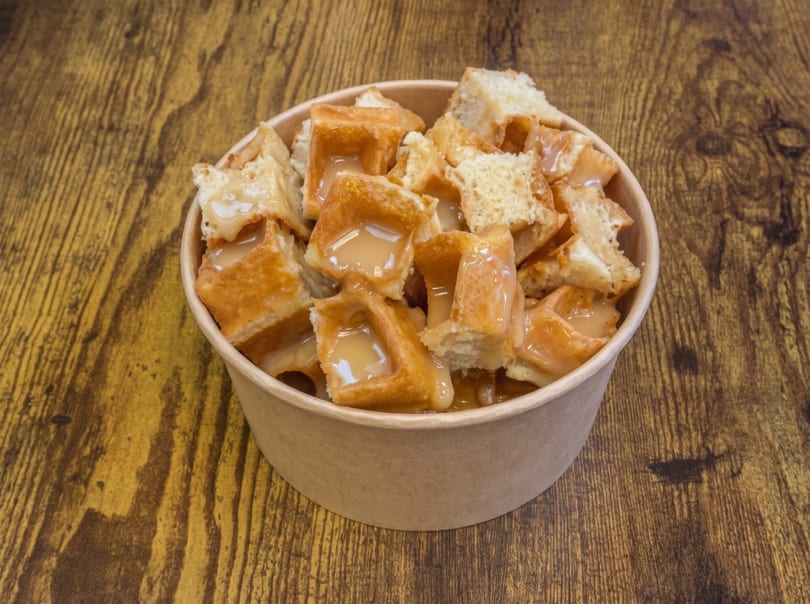 Waffle pieces with condensed milk in a paper bowl on a wooden table.